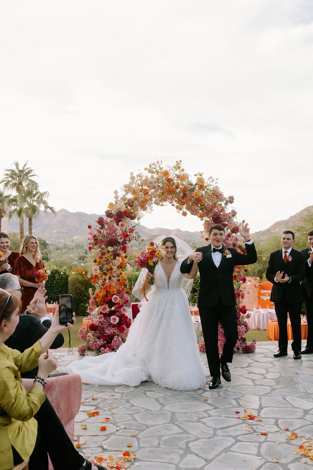 Bride and groom portrait in front of a full floral arch in vibrant pink, orange, coral and magenta blooms at an Arizona wedding