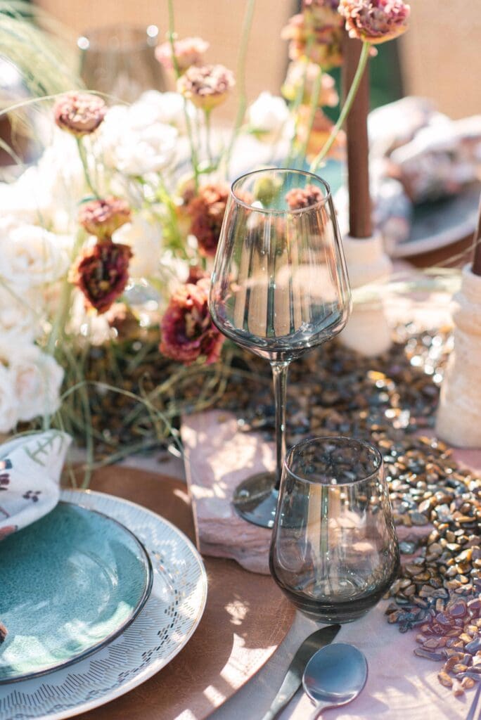 Detail shot of tiger's eye crystal chips scattered across a dusty rose linen runner beside matte black cutlery and smoked stemware