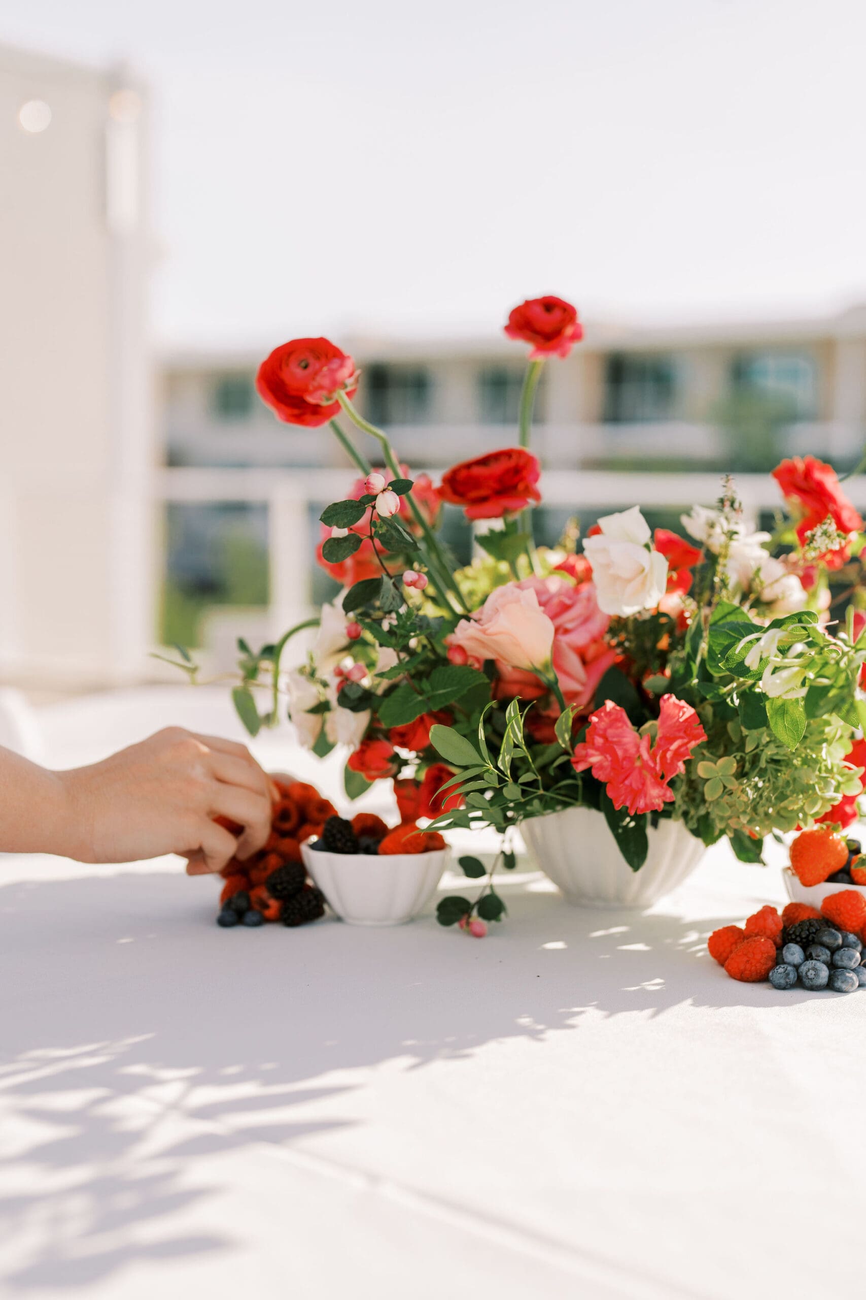 Arizona floral designer arranging vibrant red ranunculus and garden rose centerpiece with fresh berries on a studio table